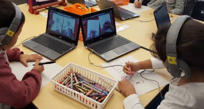 Two students drawing with crayons beside their open laptops in the same session.
