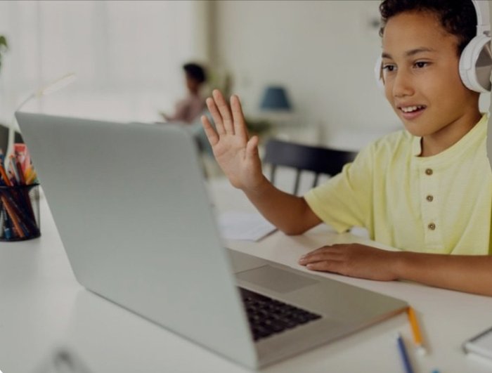 A student at home waving to their teacher on a video call.
